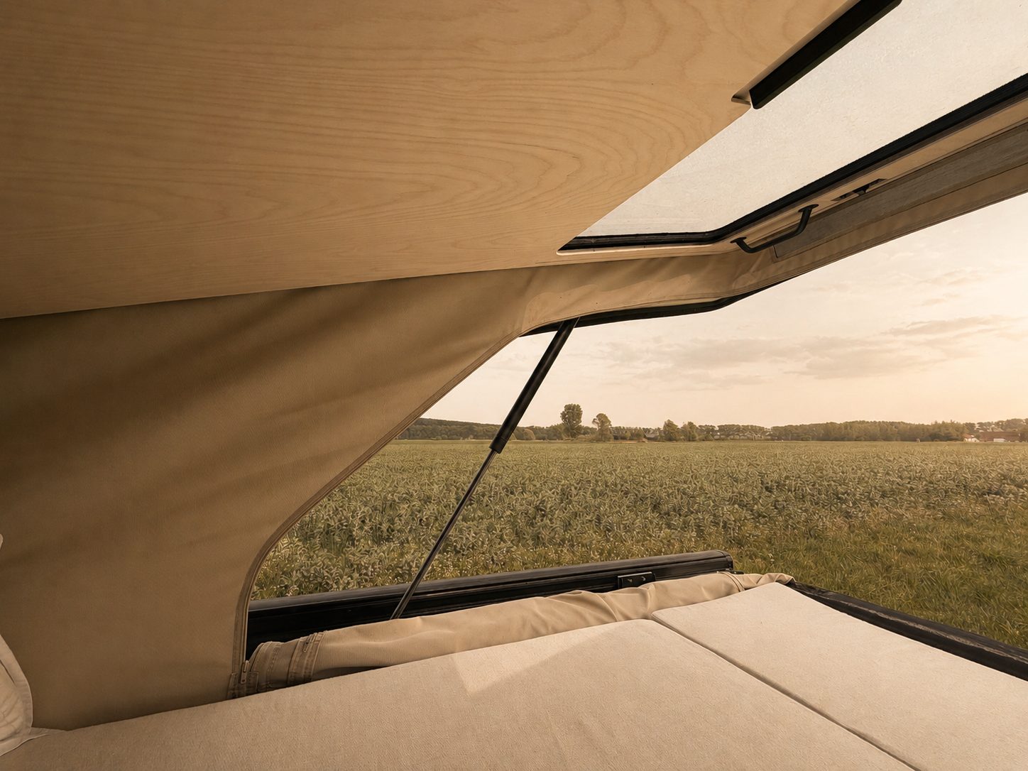 View from inside the open roof tent onto a field at golden hour