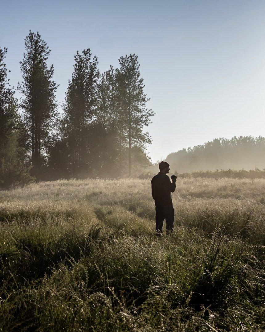 A figure with coffee in a misty field at first light